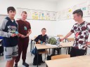 Grupa czterech uczniów - pozują przy pudełku gry "Chłopska Szkoła Biznesu", które stoi w klasie na ławce.