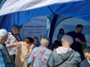 Widok z wnętrza niebieskiego namiotu promocyjnego. Grupa osób stoi przy stoisku informacyjnym i rozmawia z wystawcami