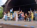 Dzieci razem z aktorami stoją na scenie muszli koncertowej