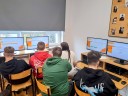 Grupa uczniów siedzi przy komputerach w pracowni.